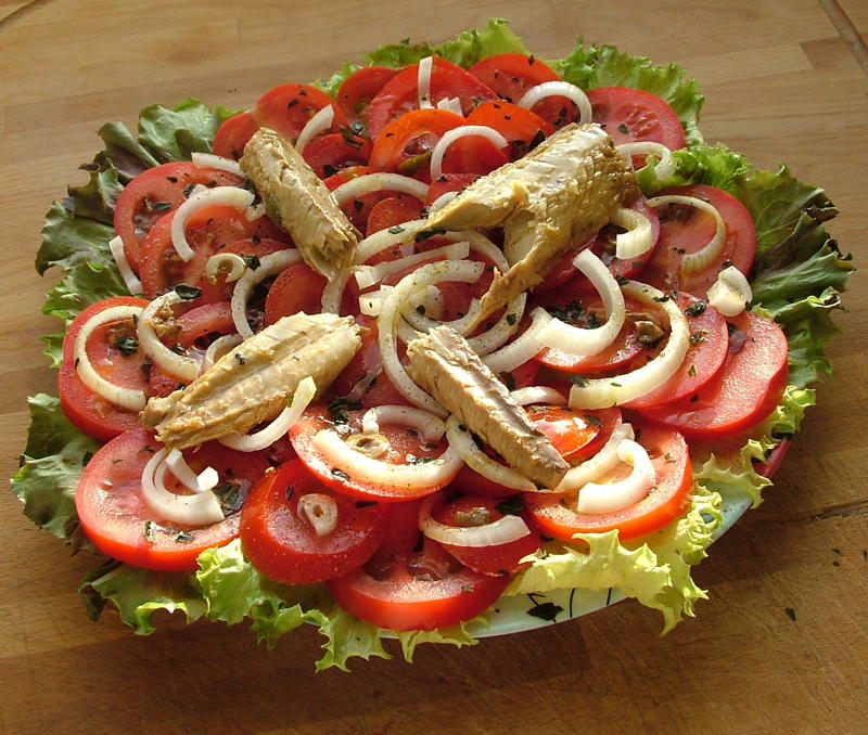 Ein Teller mit kreisförmig angerichteten Tomatenscheiben, weißen Zwiebelringen, und Dosenmakrele in Stücken