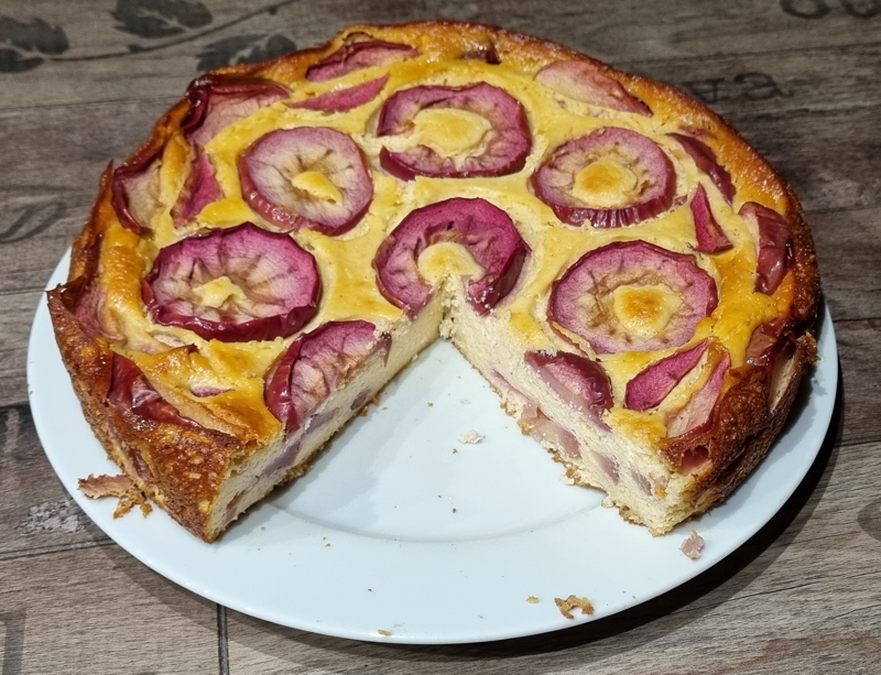 ein runder gebackener käsekuchen mit roten Apfelscheiben